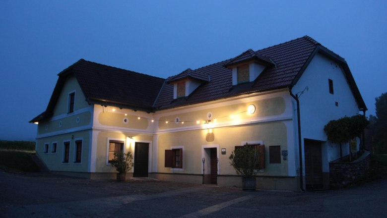 Ortmann family, © z.V.g. Fam. Ortmann A traditional, illuminated house with a yellow façade and red roof tiles at dusk.