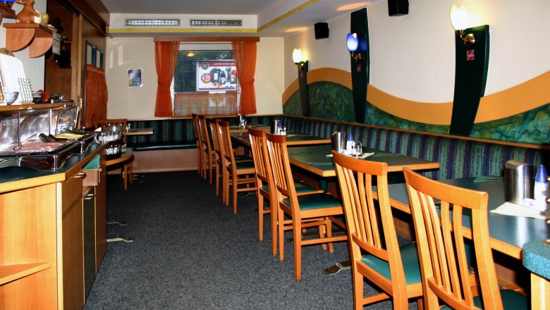Tritsch Tritsch, © Tritsch Tratsch Interior view of an empty restaurant with wooden furniture and green upholstery.