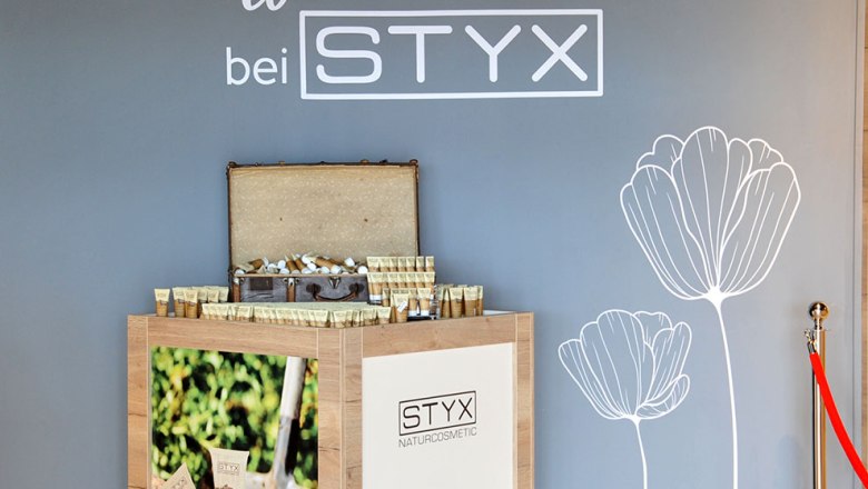 A display with STYX natural cosmetic products in front of a gray wall with a flower drawing and a welcome greeting.