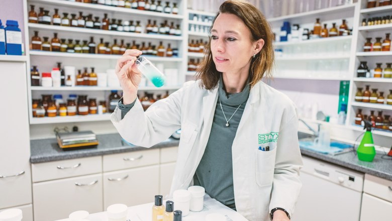 A woman in a white lab coat holds a test tube with blue liquid in a laboratory.