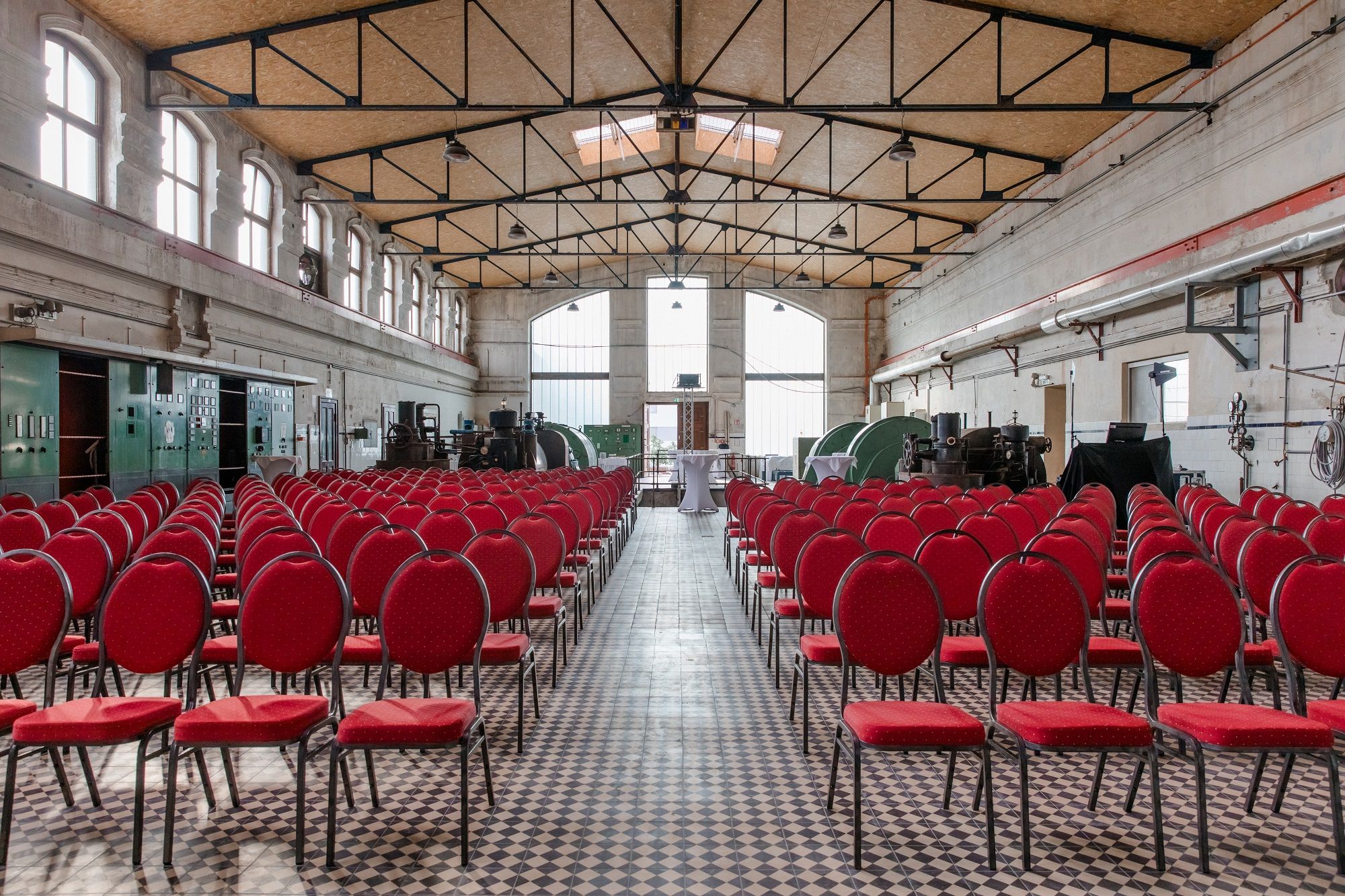 Innenansicht einer alten Turbinenhalle mit roten Stühlen und industriellen Maschinen.