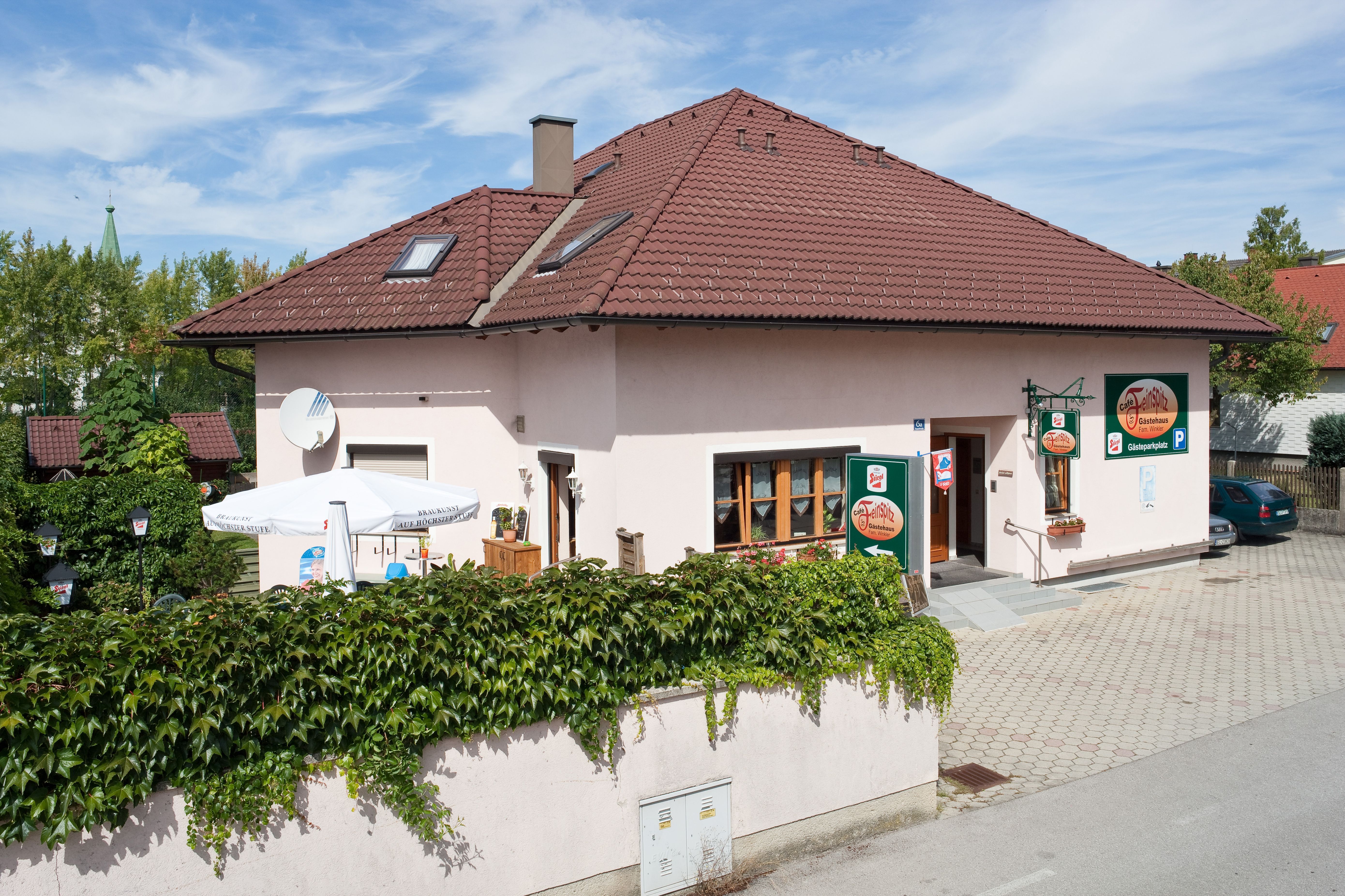 Ein Gästehaus mit rotem Dach und Terrasse, umgeben von grüner Vegetation.