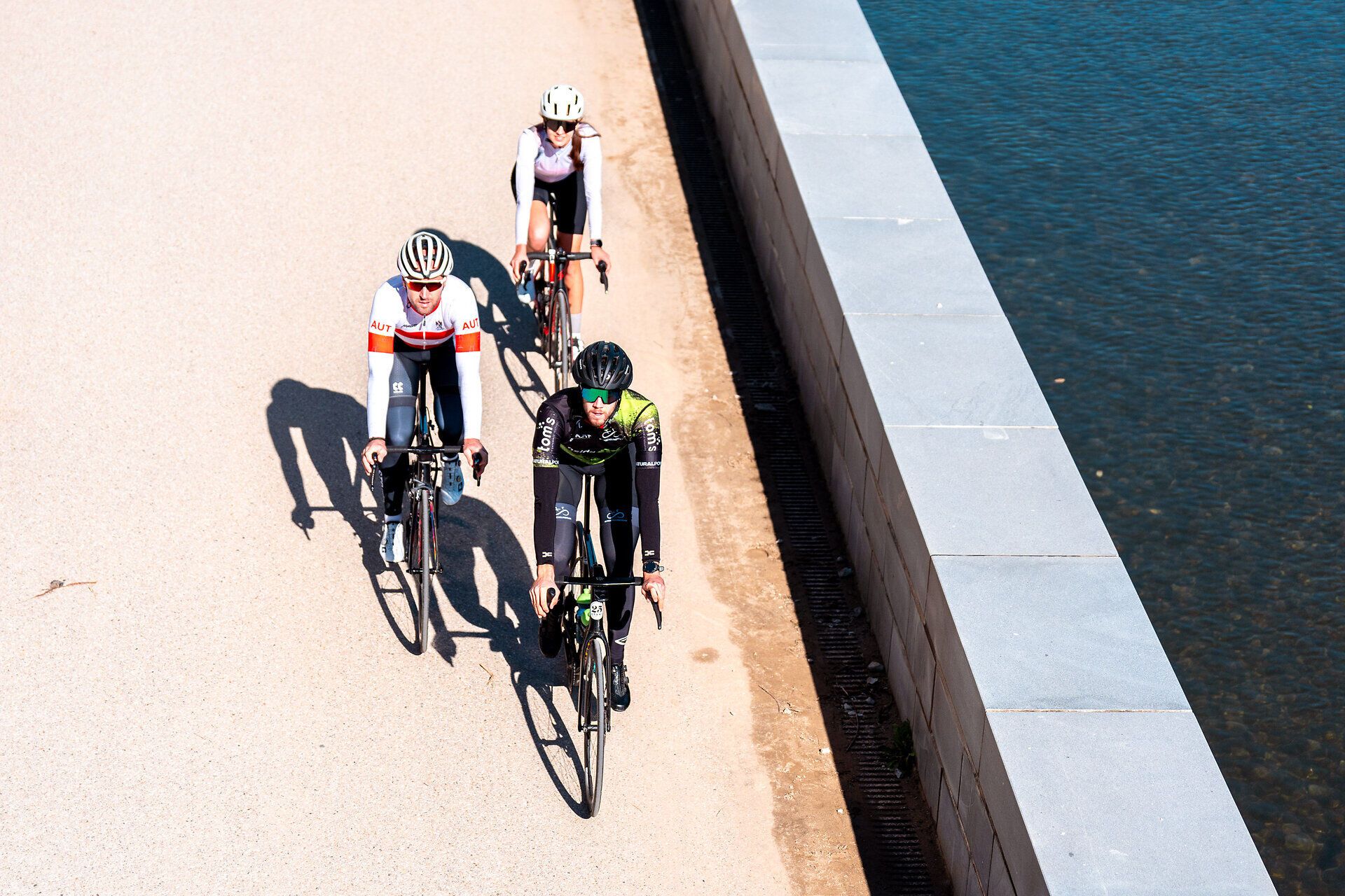 Drei Radfahrer genießen die warmen Sonnenstrahlen und die frische Luft während einer sportlichen Ausfahrt. Die malerische Umgebung lädt dazu ein, die Schönheit der Natur zu erkunden und die Freiheit des Radfahrens zu erleben. Ein perfekter Sommertag für Ausdauersportler und Naturliebhaber.
