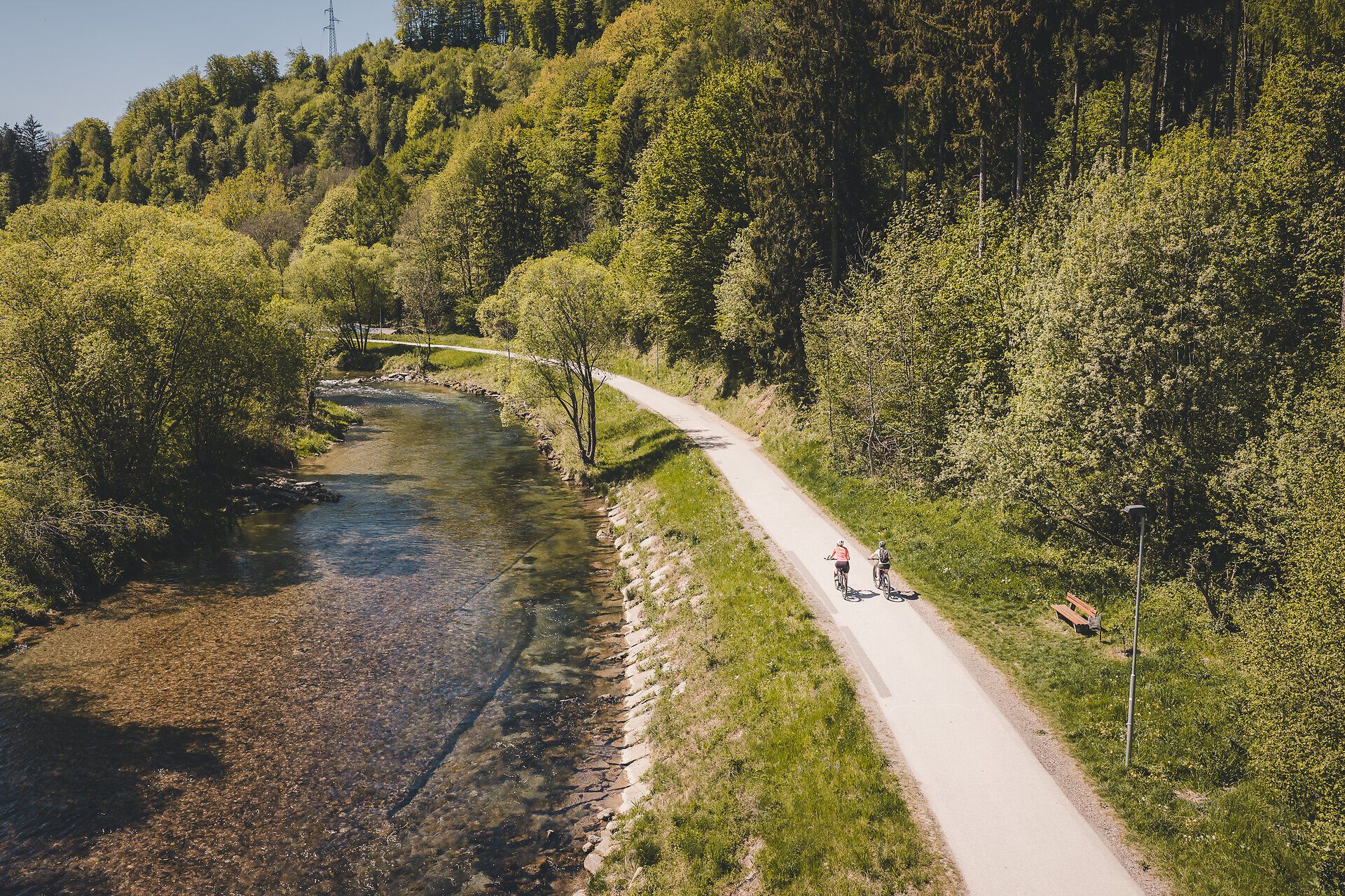 Zwei Radfahrerinnen fahren entlang des Radwegs neben einem Fluss.