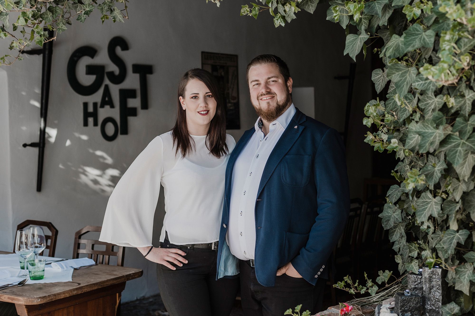Ein Mann und eine Frau stehen lächelnd vor einem Restaurant mit dem Schriftzug 'Gasthof'.