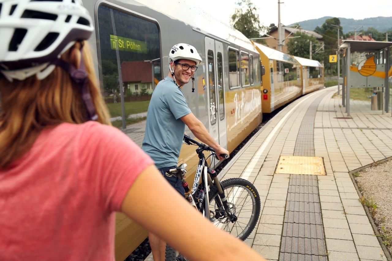 Zwei Personen mit Fahrradhelmen schieben ihre Räder am Bahnsteig, neben ihnen steht die Himmelstreppe auf den Gleisen.