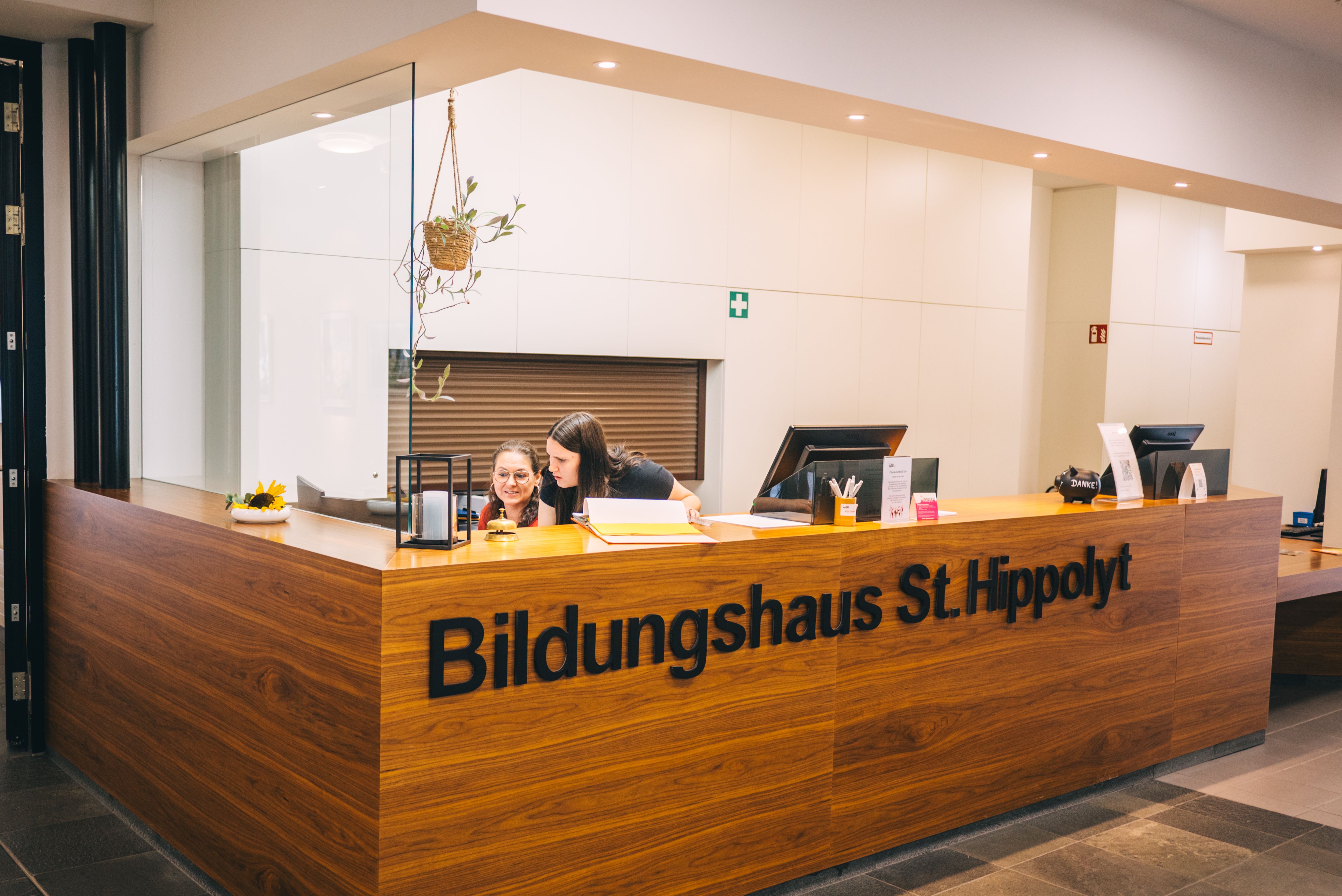 Rezeption im Bildungshaus St. Hippolyt mit zwei Personen hinter einem Holztresen.