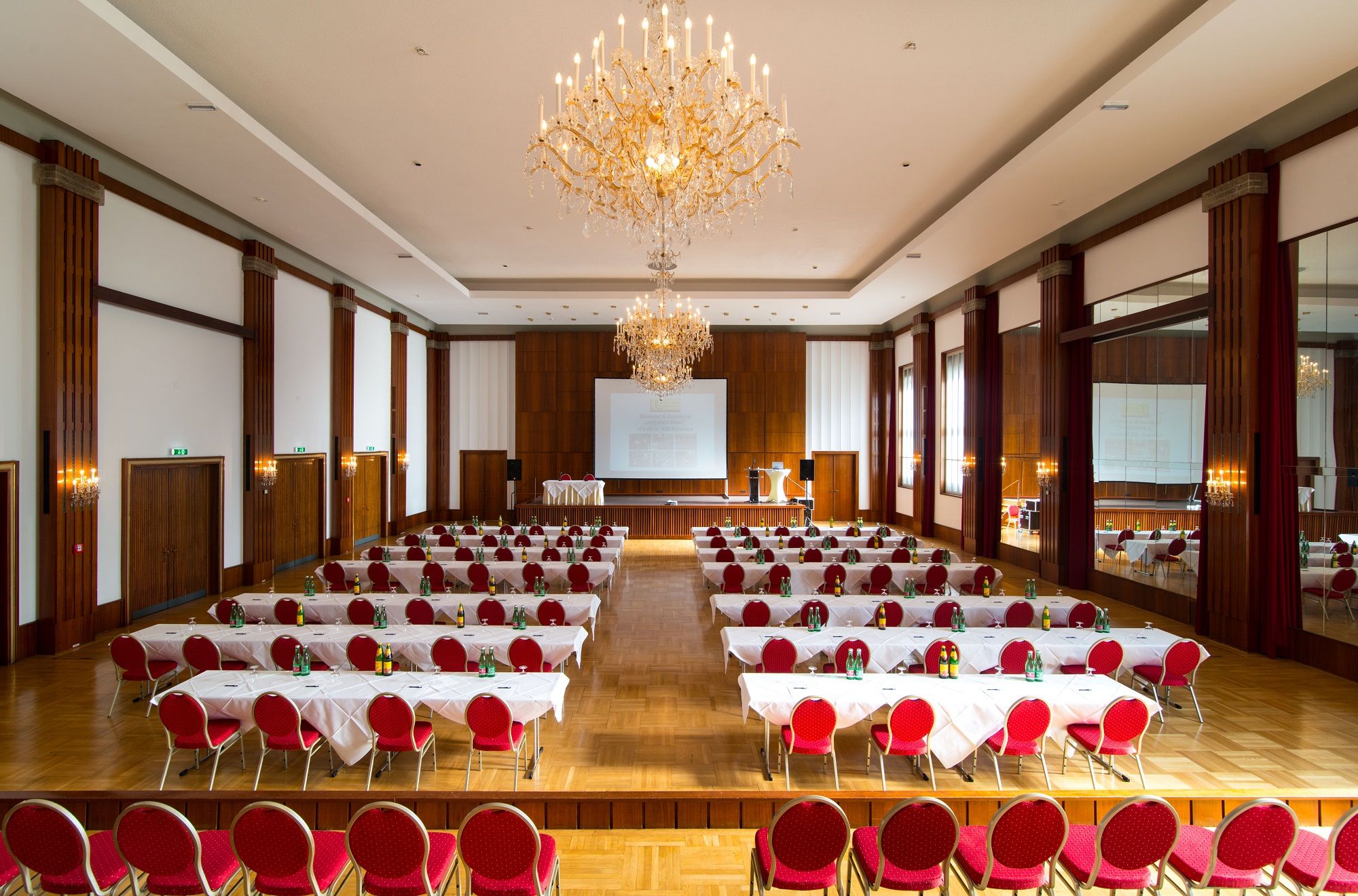 Ein großer, eleganter Konferenzsaal mit roten Stühlen, weißen Tischdecken und Kronleuchtern.