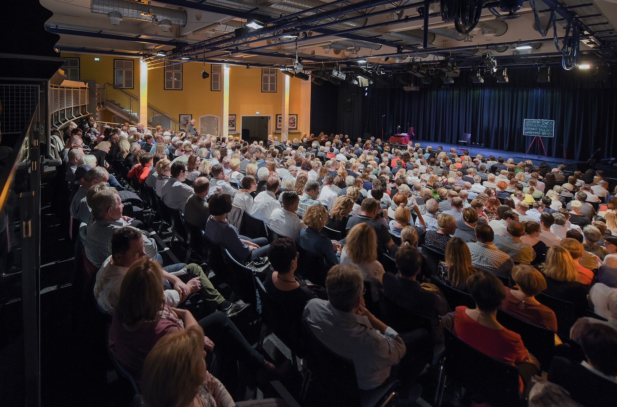 Ein gefüllter Theatersaal mit Publikum, das auf eine Bühne blickt.
