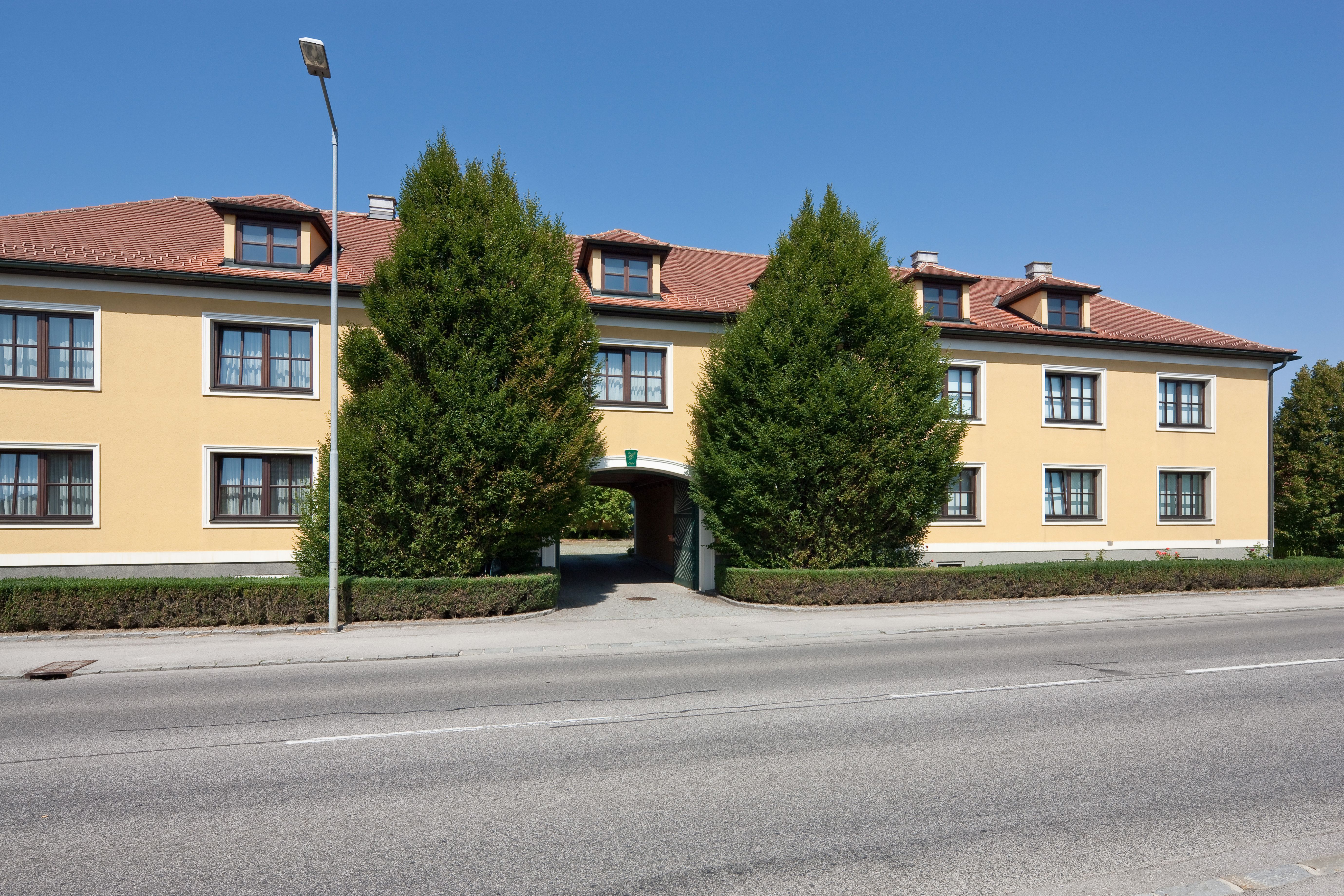 Gelbes Gebäude mit rotem Dach und Bäumen davor.