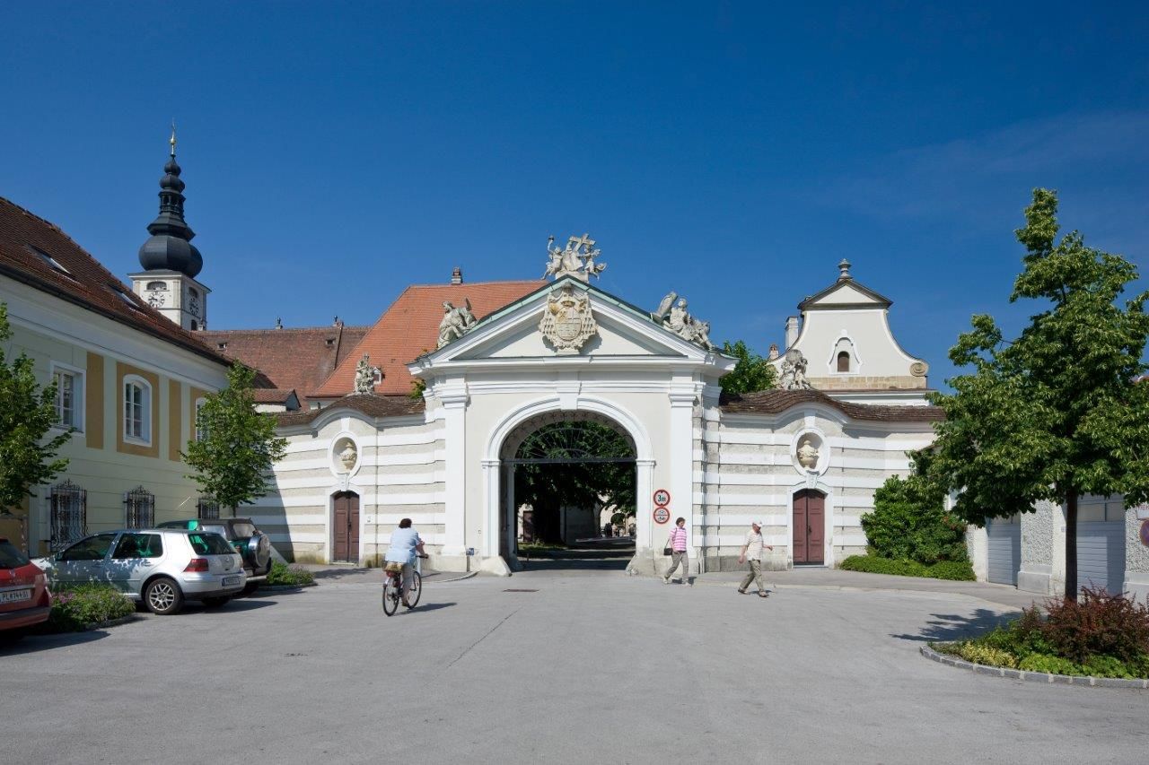 Historisches Bistumsgebäude mit Torbogen und Kirchturm im Hintergrund.