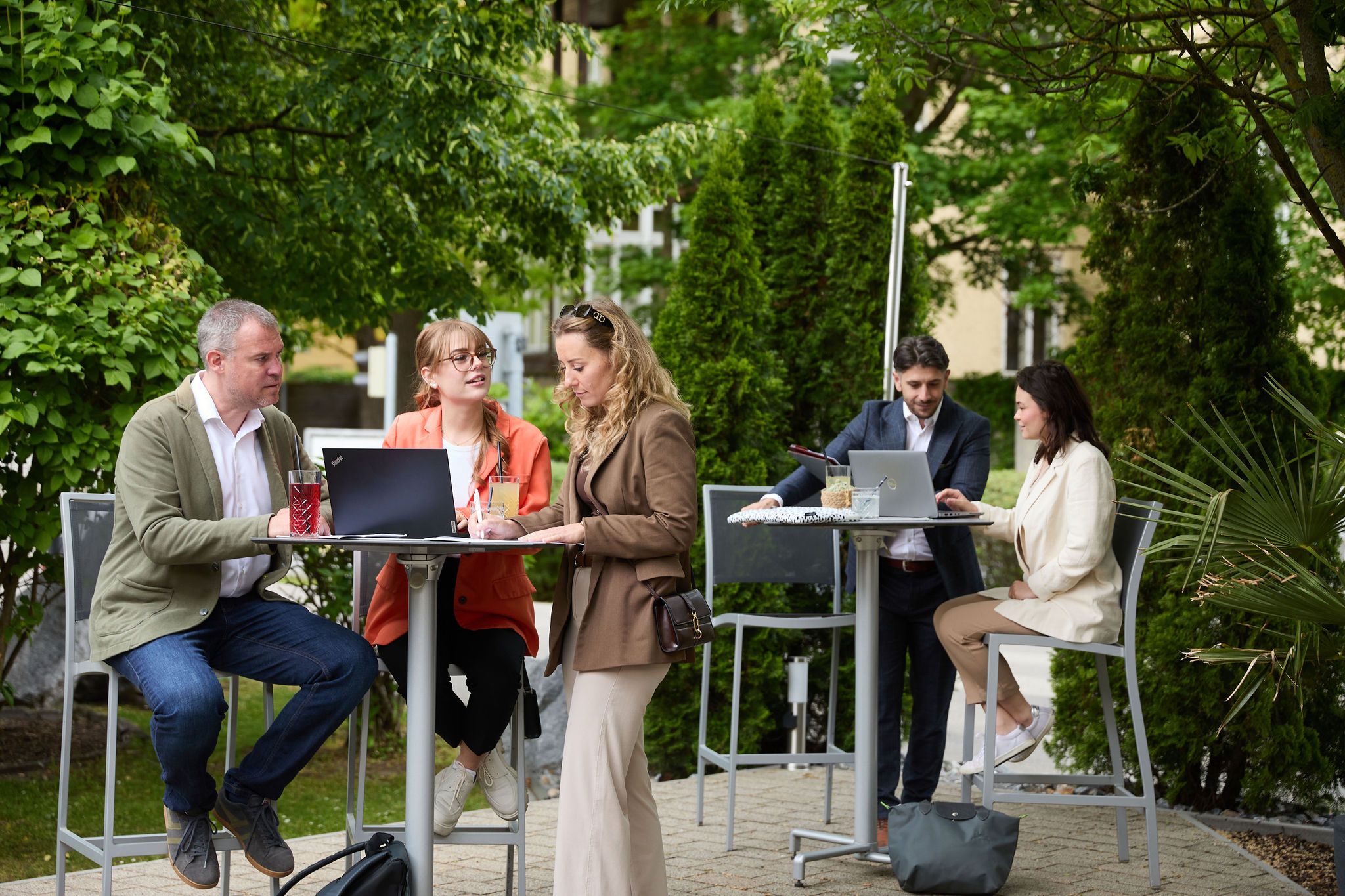 Menschen arbeiten im Freien an Stehtischen mit Laptops.