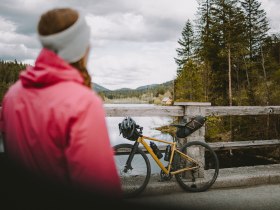 A cyclist enjoys the fresh air and breathtaking views at Hubertussee. Surrounded by dense forests and rolling hills, the idyllic landscape invites you to take a relaxing break. The calm surface of the water reflects the clouds and nature, while the gentle sounds of the surroundings create a peaceful atmosphere.