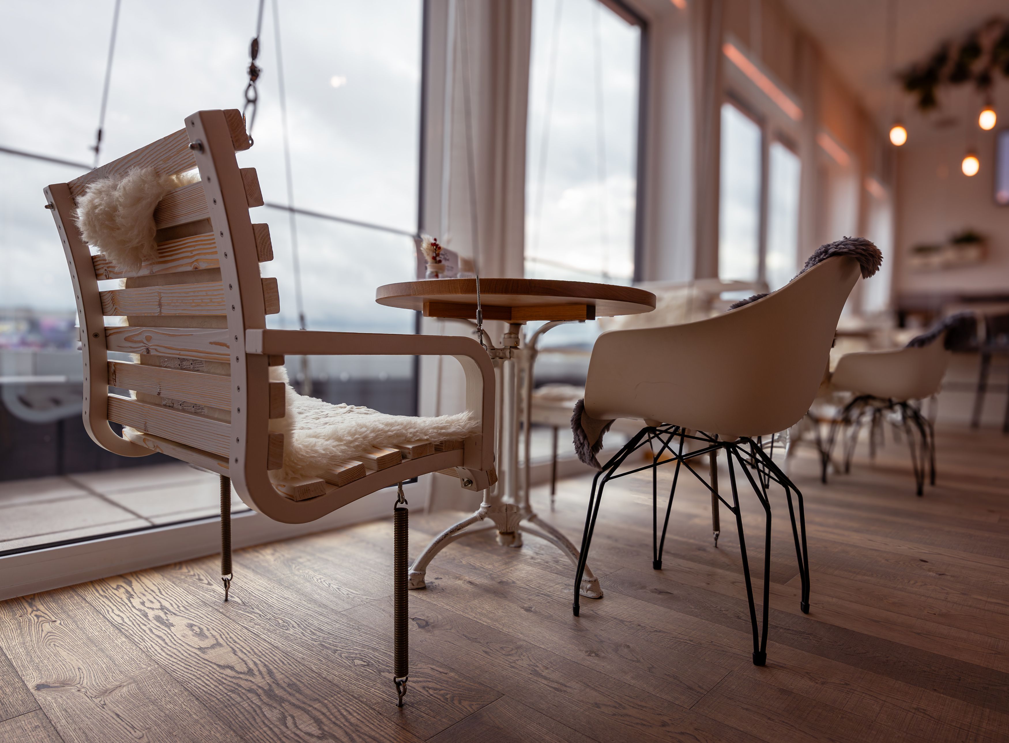 Innenansicht eines Cafés mit modernen Stühlen und Holztisch, große Fenster im Hintergrund.