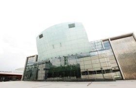 Moderne Glasfassade des Festspielhauses St. Pölten mit reflektierenden Fenstern und geschwungenem Design.