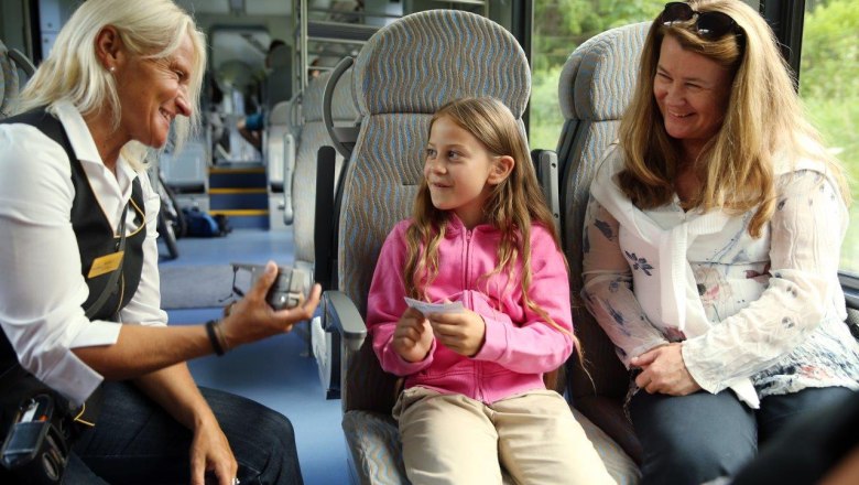 A girl smilingly hands her ticket to the conductor on the train.