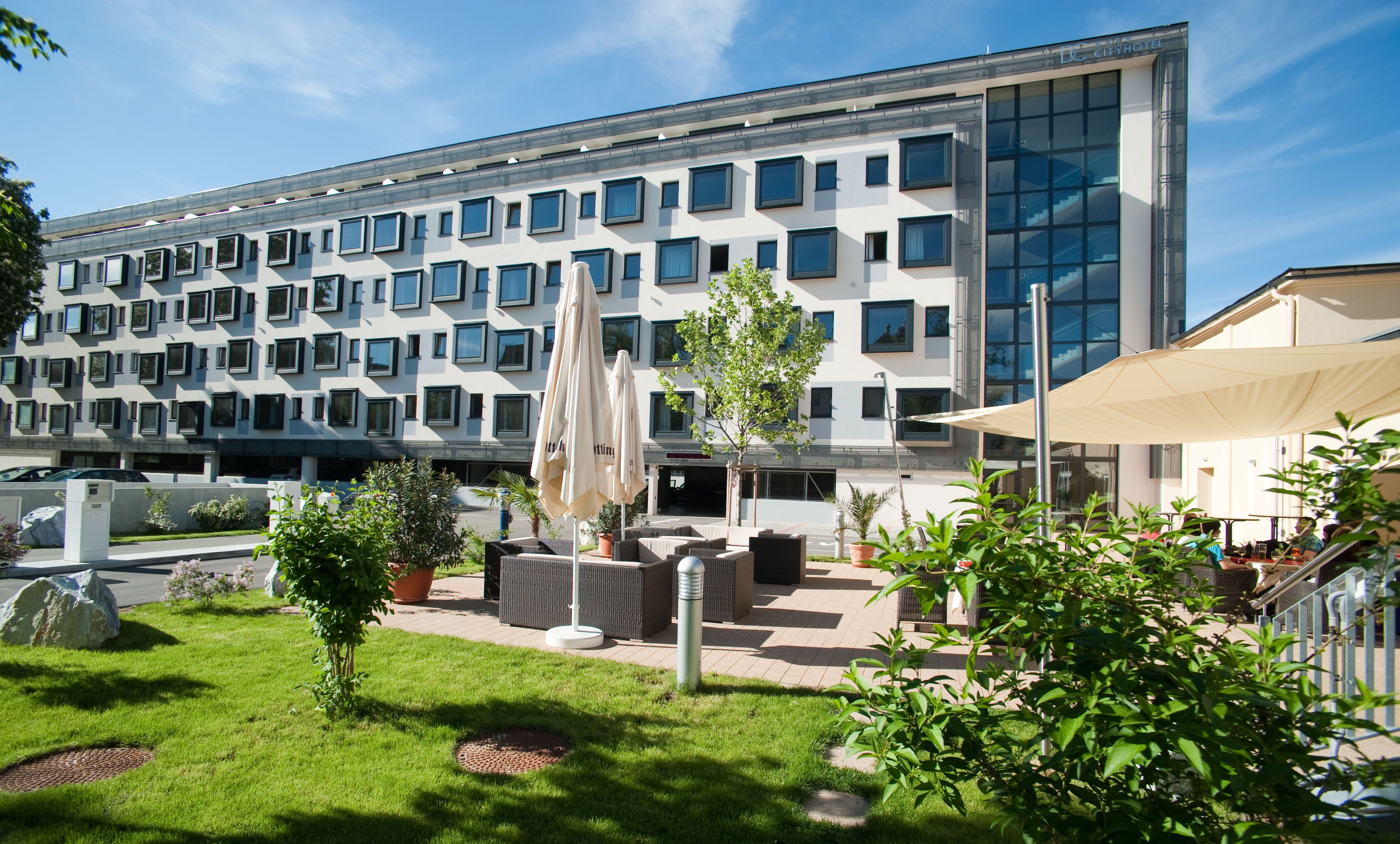 Modernes Gebäude mit vielen Fenstern und Gartenbereich mit Sitzgelegenheiten.