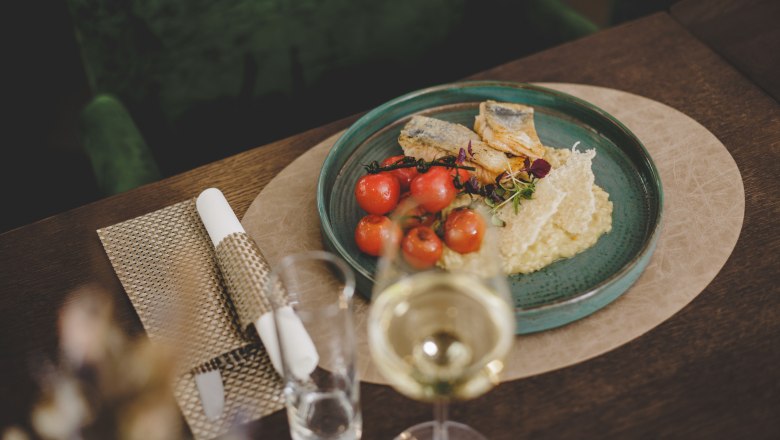 A plate of grilled gilthead bream fillet, lemon risotto and cherry tomatoes, served on a wooden table with a glass of white wine.