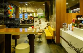 Interior view of a McDonald's restaurant with McCaf&eacute; area, seating and ordering terminals.