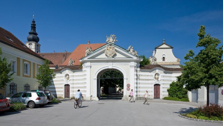 Historisches Bistumsgebäude mit Torbogen und Kirchturm im Hintergrund.