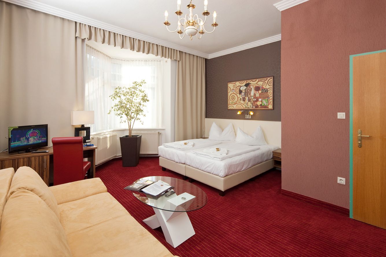 Hotelzimmer mit Doppelbett, rotem Teppich, Sofa, Fernseher und großem Fenster.