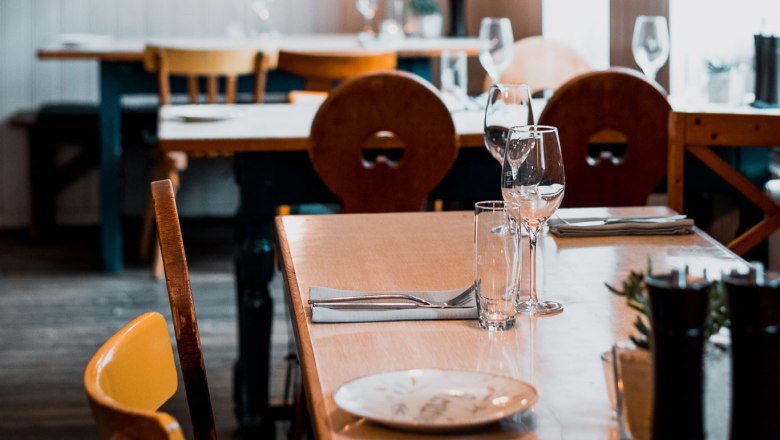 Ein gedeckter Tisch in einem gem&uuml;tlichen Restaurant mit Holzm&ouml;beln und Weingl&auml;sern.