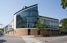 Modernes Geb&auml;ude mit Glasfassade und Ziegelmauerwerk an einer Stra&szlig;enecke.