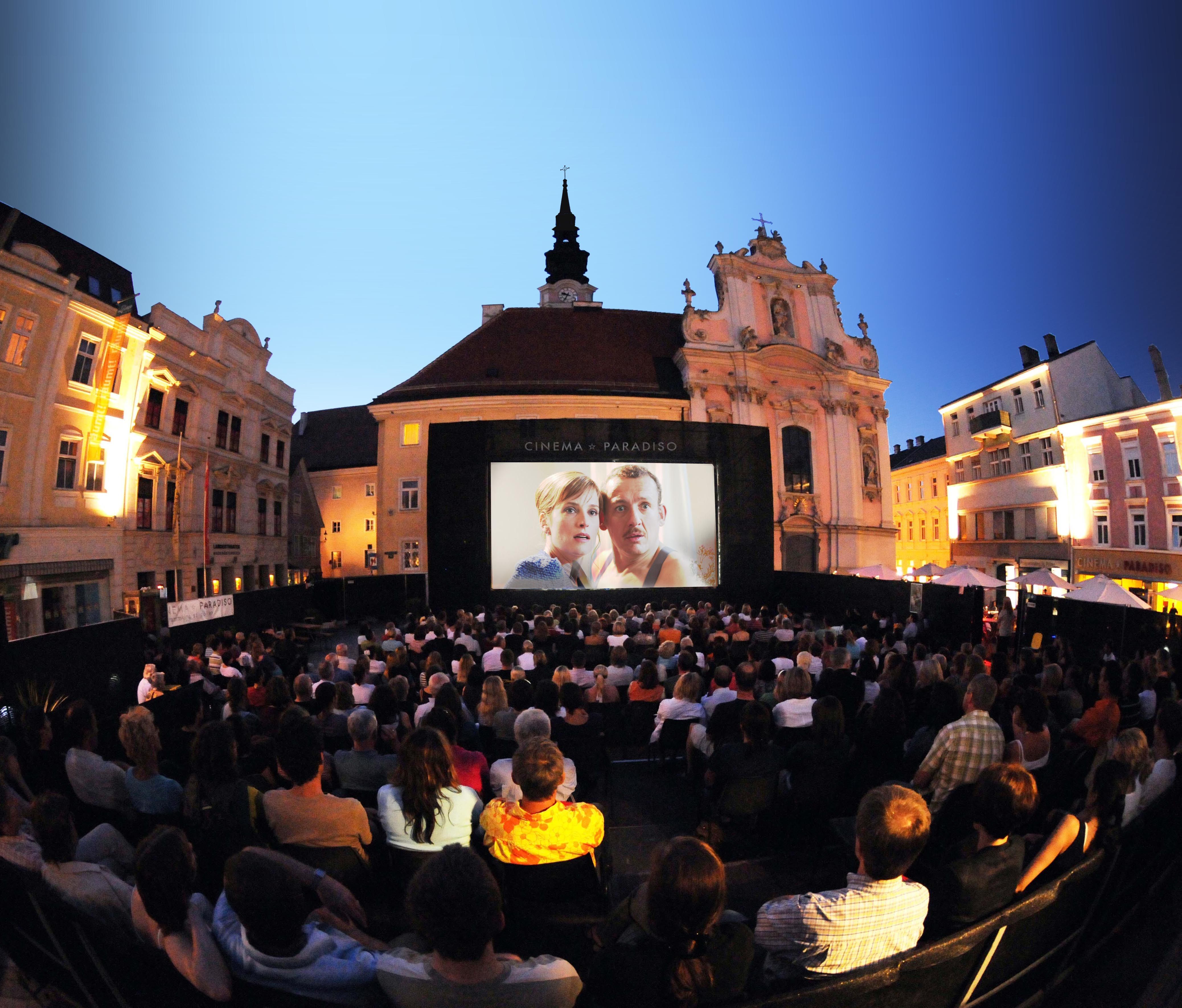 Open-Air-Kinoabend auf einem Platz mit vielen Zuschauern vor einer großen Leinwand.