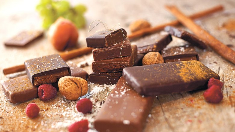 Various pieces of chocolate with nuts and raspberries on a table.