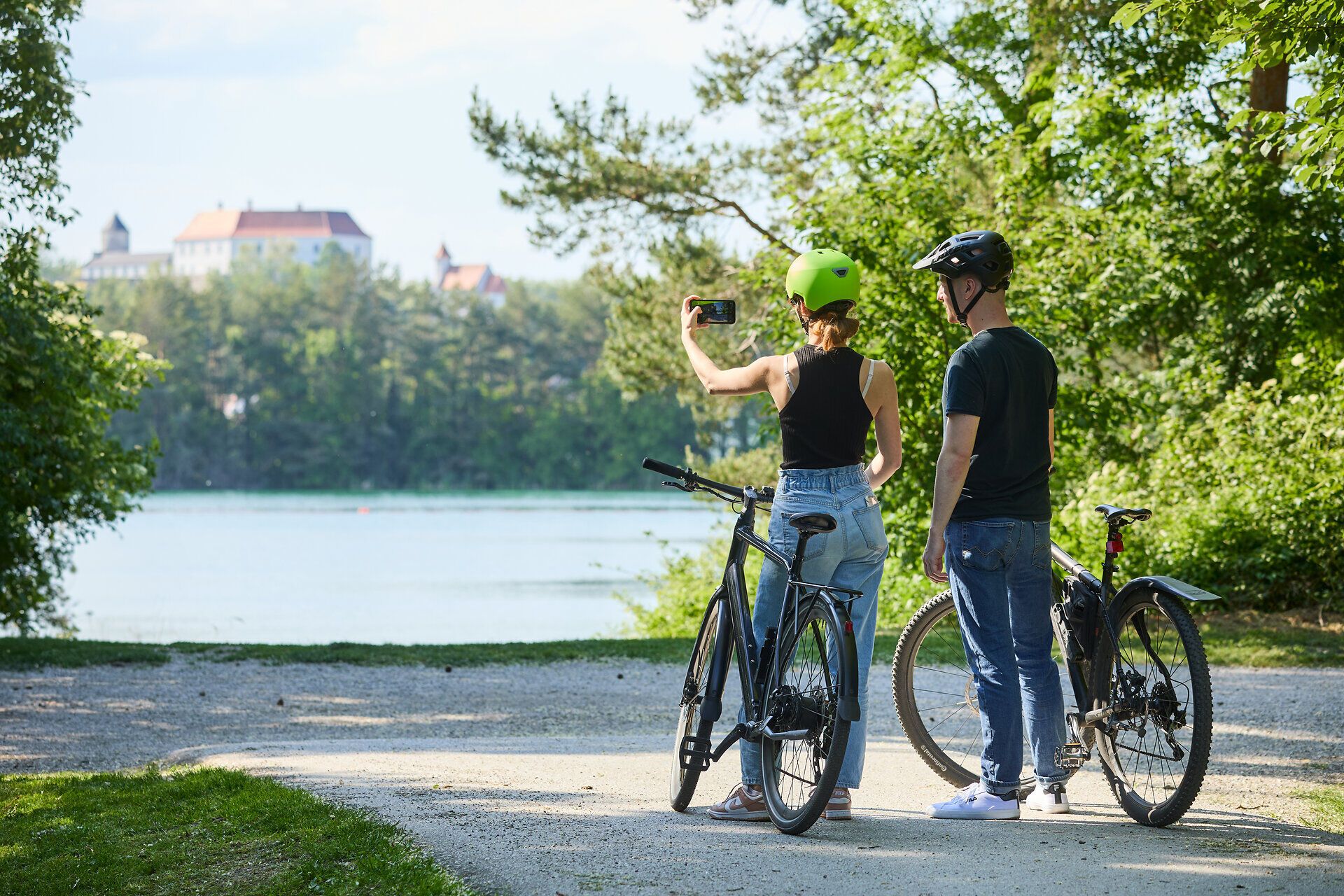 In der warmen Nachmittagssonne genießen zwei Radfahrer die malerische Aussicht auf den ruhigen See. Umgeben von üppigem Grün und dem sanften Plätschern des Wassers, halten sie einen Moment inne, um die Schönheit der Natur festzuhalten. Diese friedliche Szenerie lädt dazu ein, die Seele baumeln zu lassen und die frische Luft zu genießen.