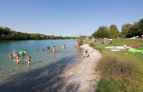 Menschen schwimmen und entspannen am Ratzersdorfer See an einem sonnigen Tag.