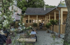 Ein gemütlicher Biergarten mit Holzmöbeln und einem Gebäude im Hintergrund.