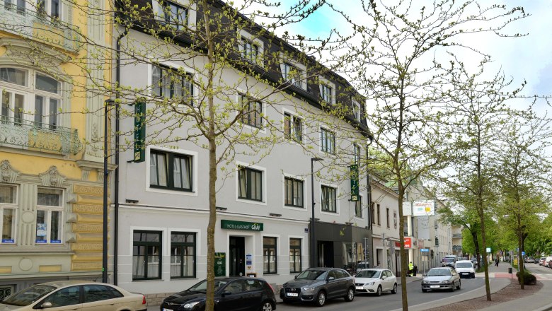 Straßenansicht des Hotel-Gasthof Graf mit parkenden Autos und Bäumen.