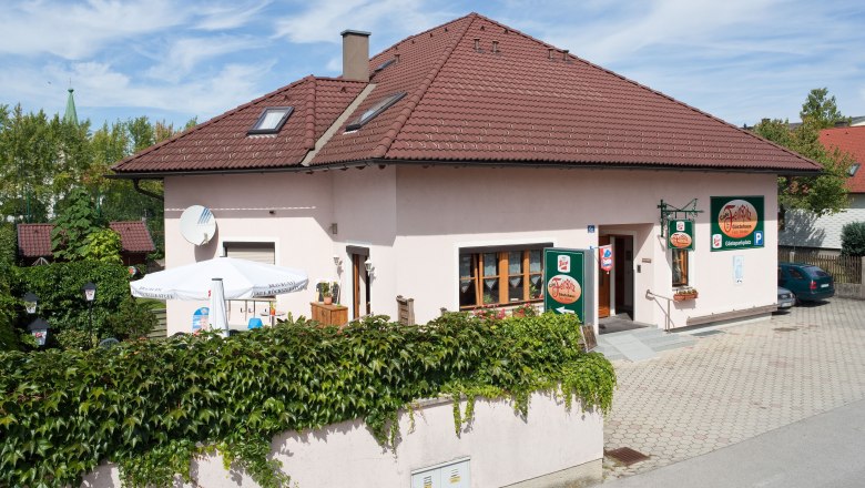 Ein Gästehaus mit rotem Dach und Terrasse, umgeben von grüner Vegetation.