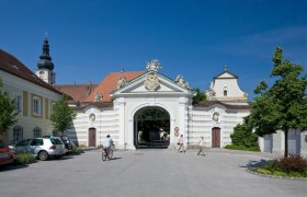 Historisches Bistumsgeb&auml;ude mit Torbogen und Kirchturm im Hintergrund.