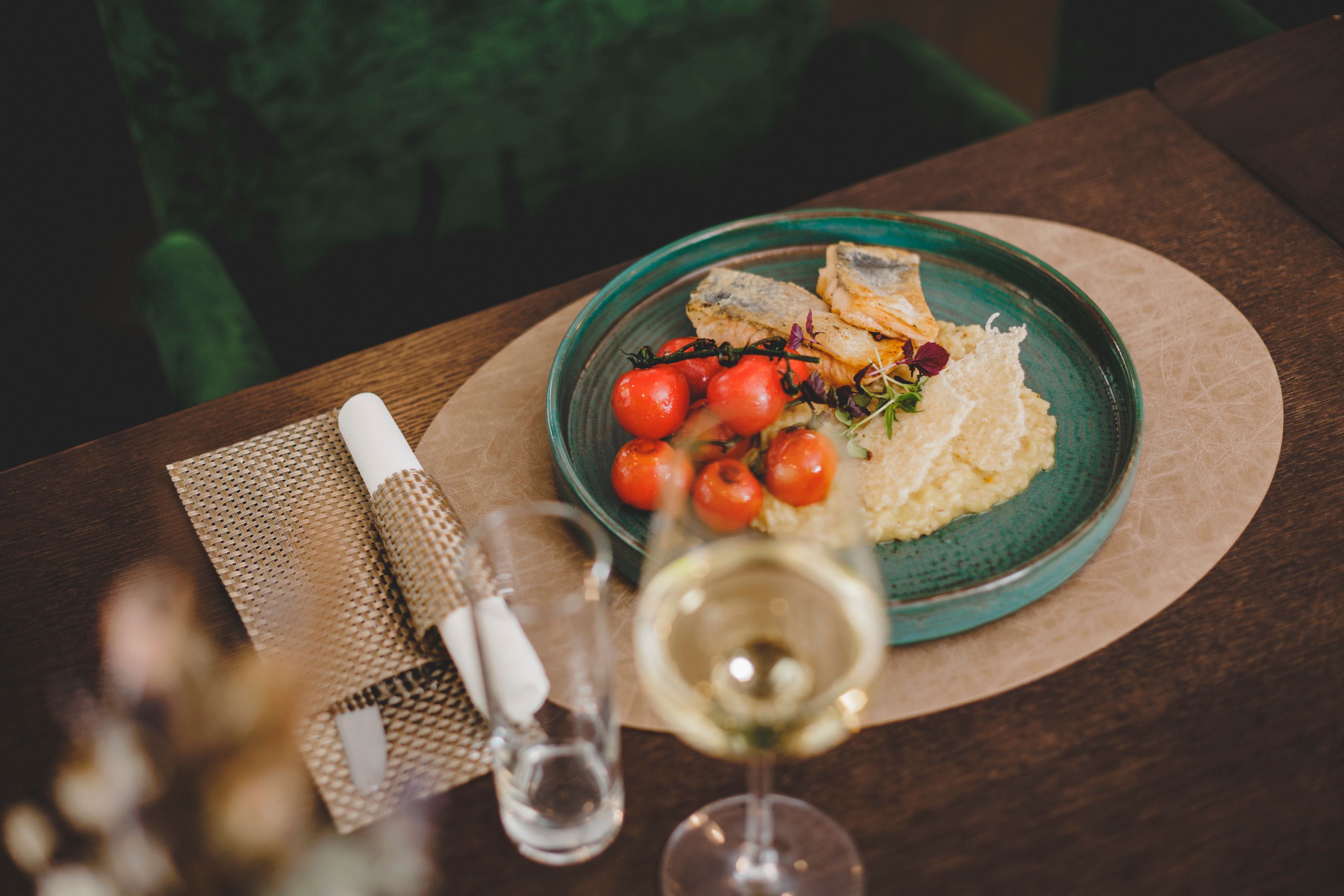 Ein Teller mit gegrilltem Goldbrassenfilet, Zitronenrisotto und Kirschtomaten, serviert auf einem Holztisch mit einem Glas Weißwein.