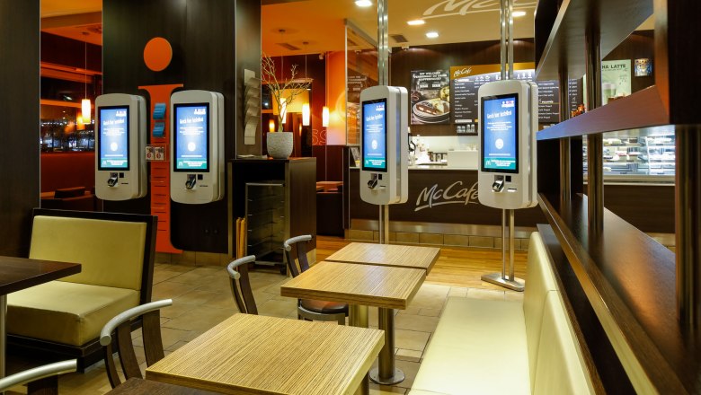 Innenansicht eines McDonald's Restaurants mit Bestellterminals und Sitzbereichen.