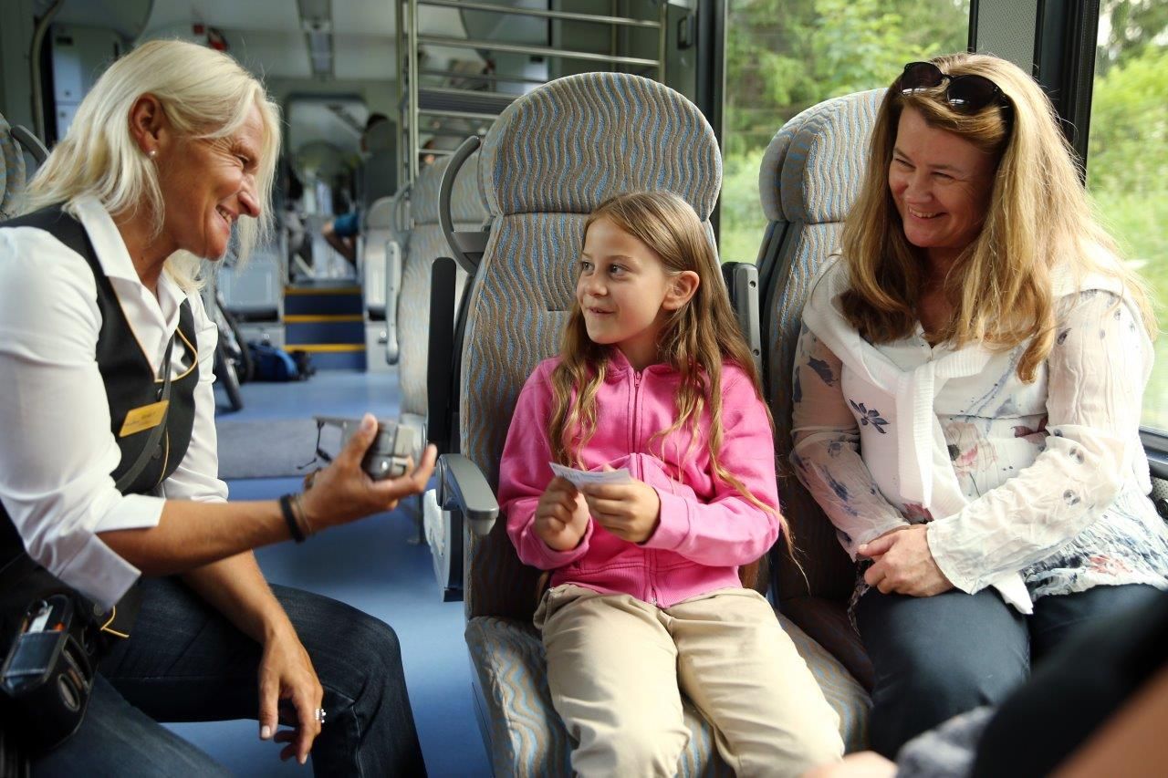 Ein Mädchen reicht der Schaffnerin in der Bahn lächelnd ihr Ticket.