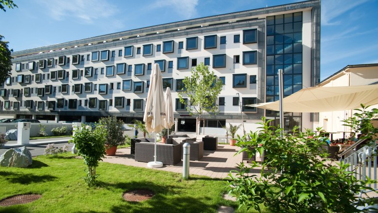 Modernes Gebäude mit vielen Fenstern und Gartenbereich mit Sitzgelegenheiten.