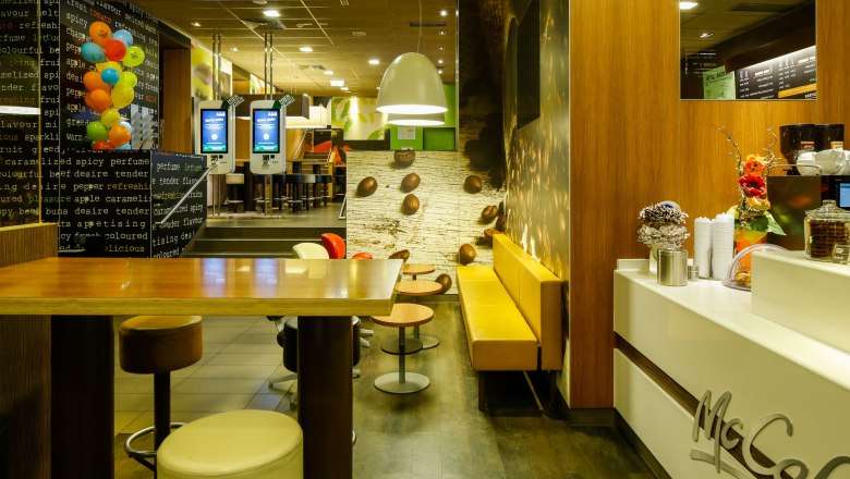 Innenansicht eines McDonald's Restaurants mit McCaf&eacute;-Bereich, Sitzgelegenheiten und Bestellterminals.