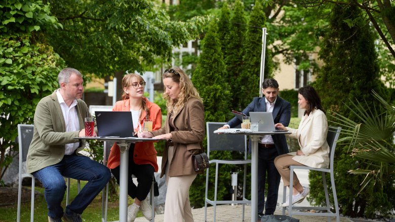 People working outdoors at high tables with laptops.