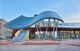 Eingang des Museums Niederösterreich mit moderner Architektur und geschwungenem Glasdach.