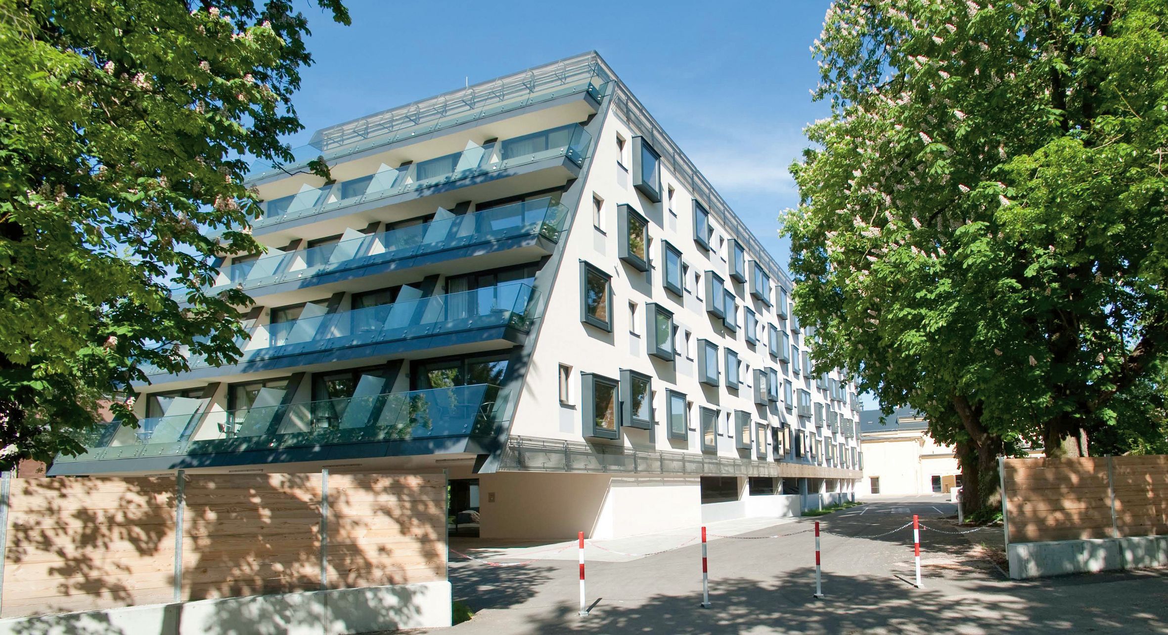 Modernes Hotelgebäude mit Glasbalkonen und Bäumen im Vordergrund.