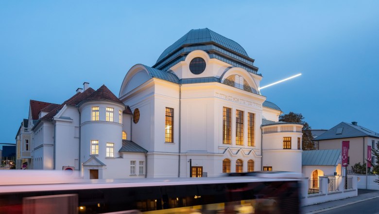 Former synagogue in St. P&ouml;lten at dusk with illuminated windows and passing bus.
