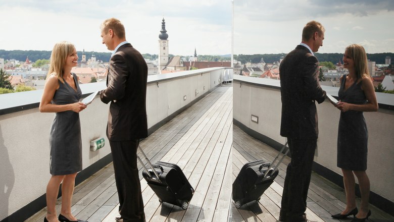 Two people are standing on a roof terrace in St. Pölten with a view of the city and talking.