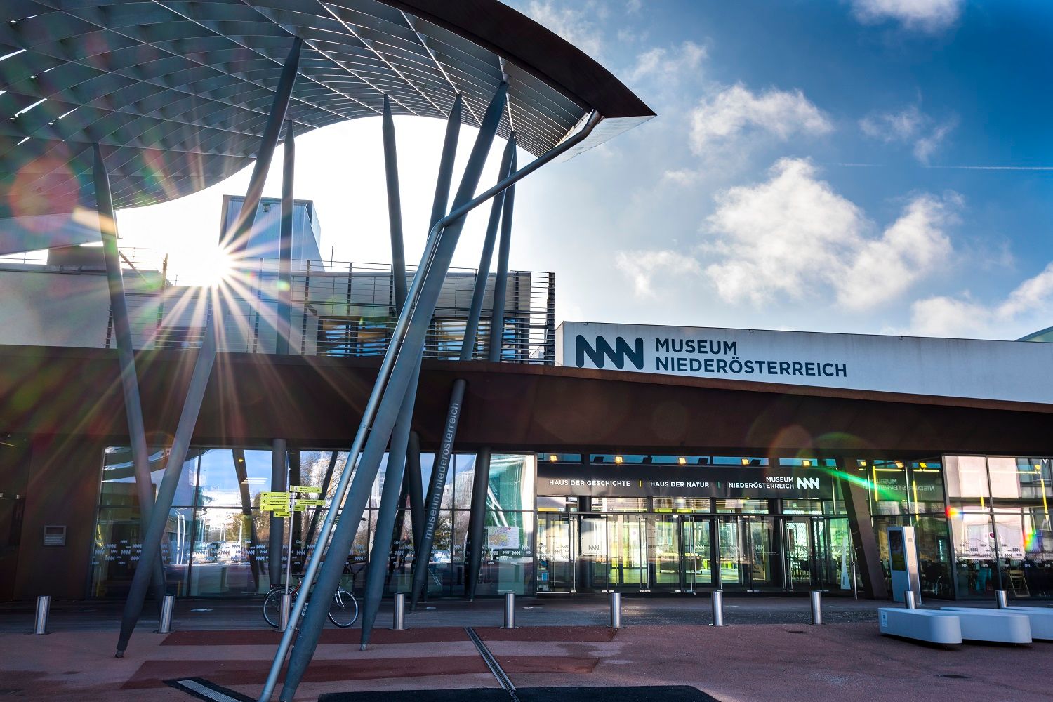 Eingang des Museums Niederösterreich mit moderner Architektur und Sonnenstrahlen.
