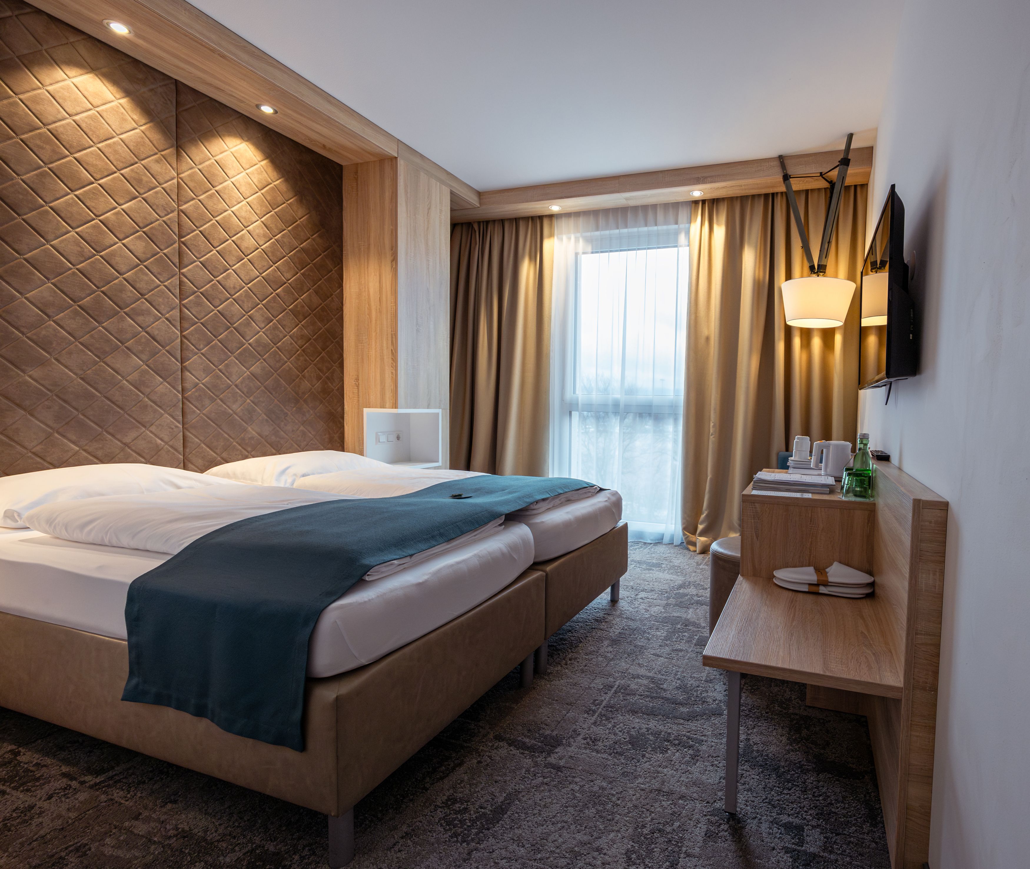 Modernes Hotelzimmer mit Doppelbett, Holzverkleidung und Fenster mit Vorhängen.