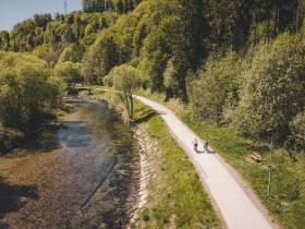 Two cyclists ride along the cycle path next to a river.