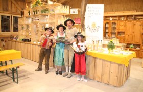 A family in traditional dress stands in a store with products and a banner reading 'The Quail's Egg'.