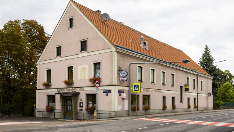 Ein traditionelles Wirtshaus mit rosa Fassade und roten Dachziegeln an einer Stra&szlig;enecke in Pottenbrunn.
